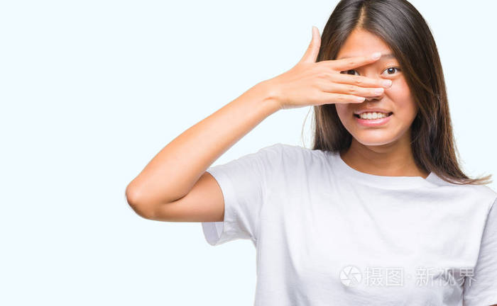 年轻的亚洲女人在孤立的背景下偷看,震惊地遮住脸和眼睛,用手透过手指