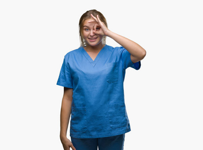 年轻的高加索护士女士穿着外科医生制服，在孤立的背景上做着OK的手势，用手微笑的眼睛透过手指看着幸福的脸。