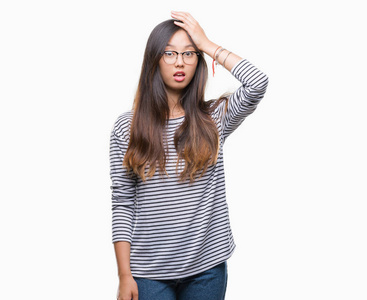 年轻的亚洲女人戴着眼镜，在孤立的背景上惊讶地用手在头上，因为错误的记忆错误。 忘记了糟糕的记忆概念。