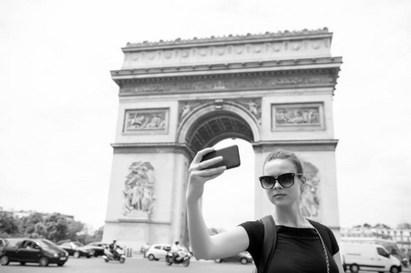 法国巴黎拱门纪念碑上有智能手机的妇女。在凯旋门, 女人用电话做自拍。在法国首都度假和观光。时尚外观和感官美的女孩