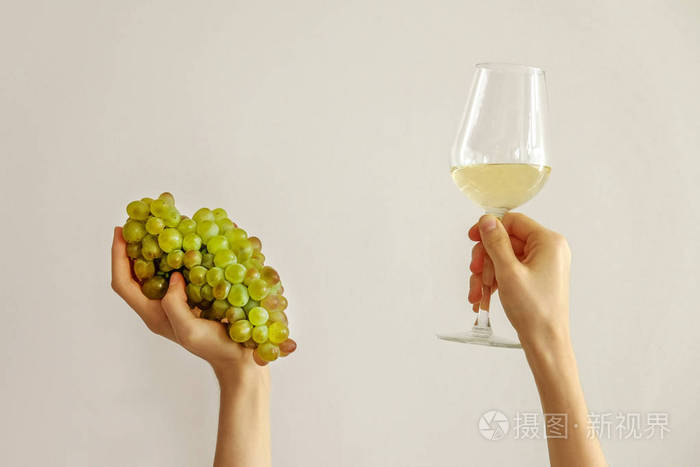 一只手握着昂贵的哈多奈葡萄酒的酒杯,另一只手拿着一串成熟的白葡萄