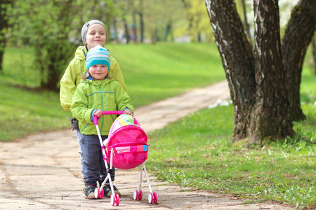 儿童的友谊。小朋友。孩子们在绿色公园散步。小男孩和女孩的玩具马车娃娃。兄妹在一起