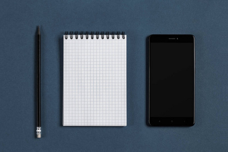 空白记事本黑色手机和蓝色背景上的铅笔