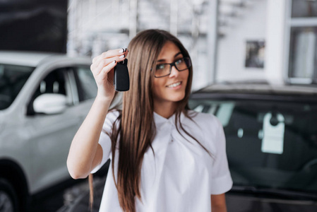 一个年轻漂亮的女人的肖像，看着车上的相机，展示着钥匙。