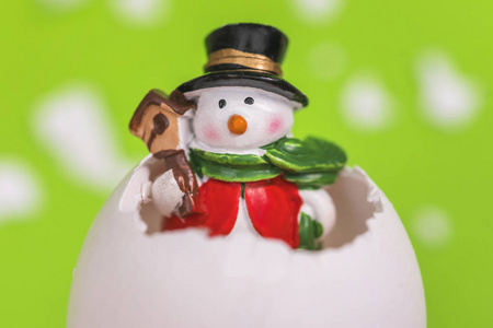 绿色背景上白色蛋壳里的小玩具雪人