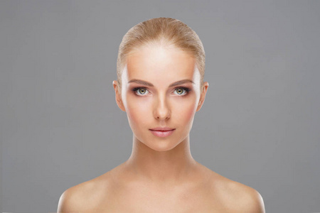 年轻健康的女人在灰色背景下美丽的脸。 护肤化妆品和面部提升概念。
