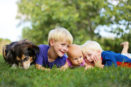 三个年幼的兄弟姐妹一个年幼的孩子，他的弟弟和他的小妹妹夏天和他们收养的德国牧羊犬一起在外面的草地上放松。