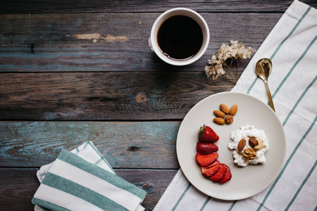 在木桌上放一盘奶酪草莓和坚果一杯咖啡和毛巾健康食品早餐