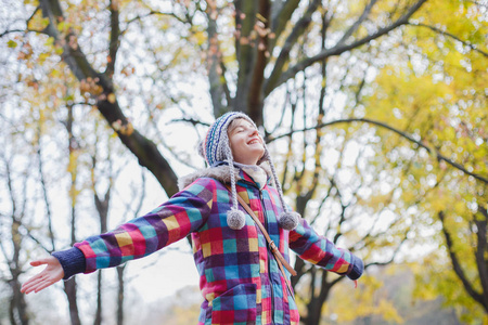 美丽的年轻女子戴着帽子，双手伸在秋天的森林里