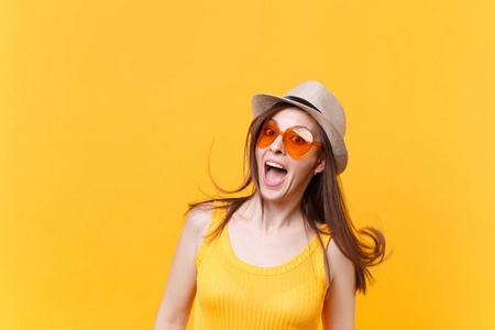 兴奋微笑的年轻女子的肖像，戴着稻草夏帽，橙色的眼镜，在黄色的背景上隔离飘扬的头发复制空间。 人们真诚的情感生活方式观念。 广告区