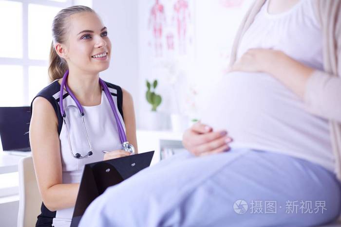 女医生用听诊器和片剂与孕妇在医院交谈