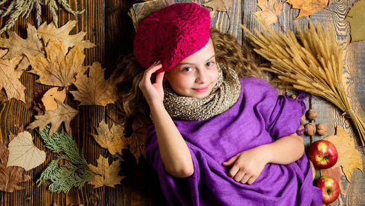 时尚小女孩穿针织帽子贝雷帽和围巾。秋季时尚饰品的概念。时尚潮流秋季季。孩子躺在木背上落下叶子的顶部景色。针织配件时尚细节