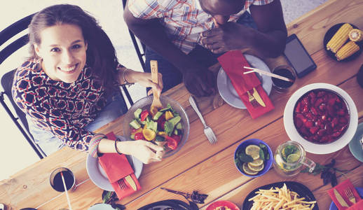 顶视图的一群人在一起时坐在木桌吃饭。在桌子上的食物。人们吃快餐