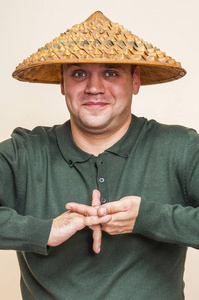 人类的脸可能与强烈的表情和情感不同。 微笑的男人戴着亚洲草帽，露出奇怪的手势。