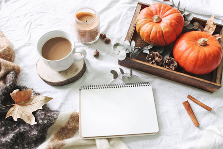秋季早餐在床上组成。 空白日历笔记本模型。 一杯咖啡，桉树叶和南瓜在木制托盘上。 白色亚麻布背景。 感恩节万圣节假日顶部景观。