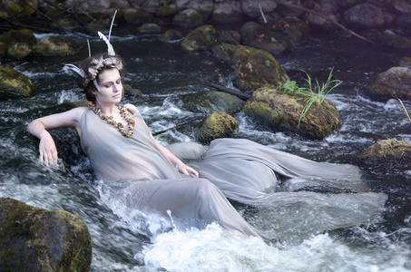 河中的仙女穿着灰色的丝绸连衣裙，一条海螺壳项链和一件佩雷维西德的头饰，躺在他的河里