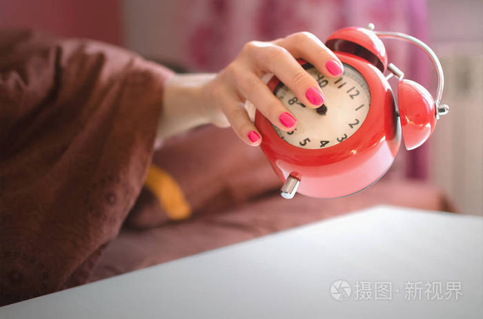 睡懒觉的女人在早上试图关掉桌子上的红色闹钟
