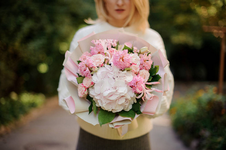 穿着白色汗衫的女人手里拿着一大束粉红色的嫩花，上面装饰着绿叶