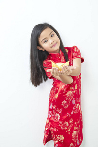 8岁的女孩子穿着中国传统服装2019年新年，手持一个金锭站在白色的墙壁背景上