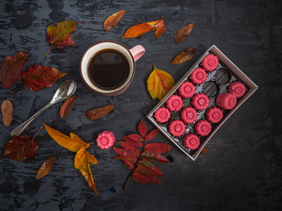一杯茶，一盒巧克力，草莓软糖，在黑色的木制背景上被彩色的秋叶包围着