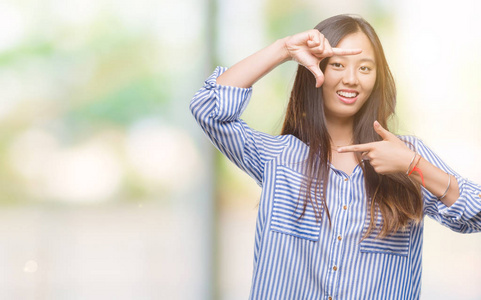 年轻的亚洲女人在孤立的背景上微笑，用手和手指制作框架，用快乐的脸。创意和摄影理念..