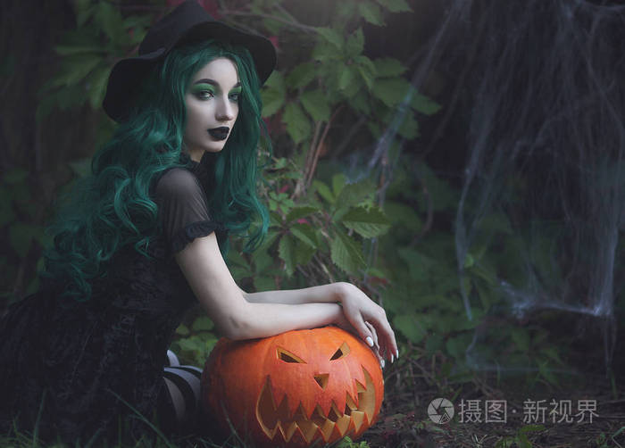 万圣节女巫绿色的头发拿着一个雕刻的可怕的南瓜漂亮