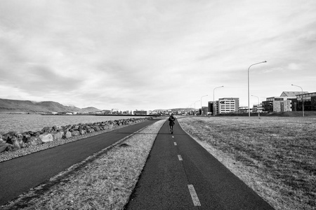 在冰岛雷克雅未克的多云天空上, 妇女沿着海面行走。海滨漫步于城市景观。城市景观的旅游和流浪。自由前景和未来