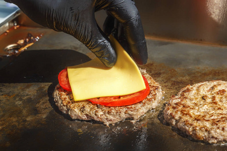 s hand puts the cheese on a meat burger that is cooked on the gr