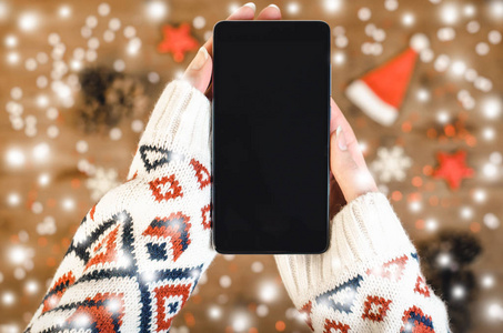 女性手拿智能手机，在木制背景上用OLED显示，带有圣诞礼物雪花和雪魔法童话的光效果。新年快乐和圣诞节平躺构图的顶部视图。