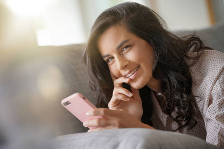 黑发女人在沙发上放松，与智能手机相连