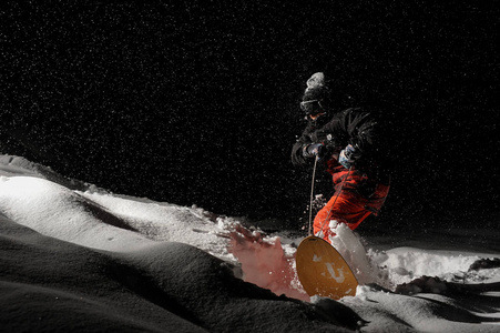 穿着黑色和橙色运动服的职业滑雪者在黑夜骑着雪粉山