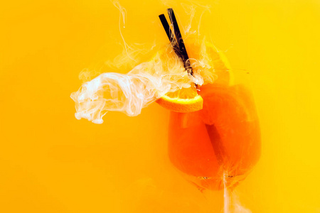 在橙色背景下，在水中的玻璃中加入锥虫鸡尾酒。 橙汁在水下面有红色和白色丙烯酸涂料。