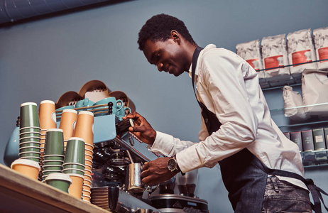 在白色衬衫和围裙的非洲裔美国咖啡师的侧面视图制作咖啡与咖啡机