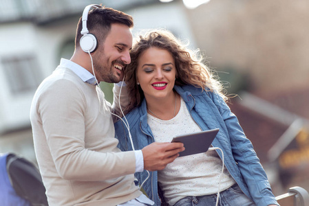 快乐的年轻夫妇带着平板电脑和耳机在城里享受音乐。