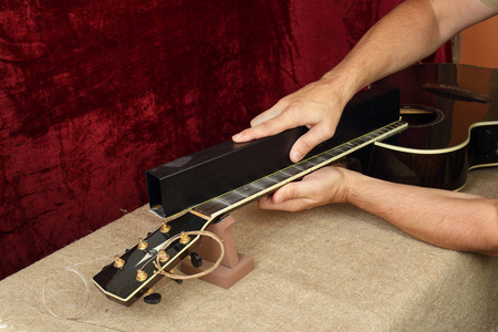 乐器吉他修理和服务工人研磨黑色声学吉他颈部烦恼。