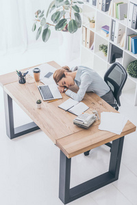 过度劳累的成年女商人睡在工作场所的视角