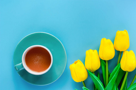 一杯带有茶托和人工黄色郁金香的蓝色背景咖啡，用于饮料和饮料概念