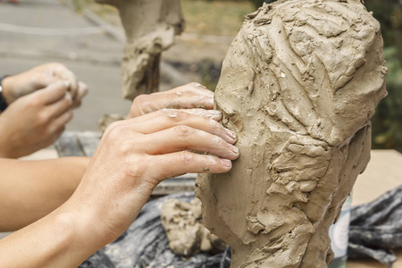 雕塑家创造了一个半身像，并把他的手黏土放在雕塑的骨架上。 近点