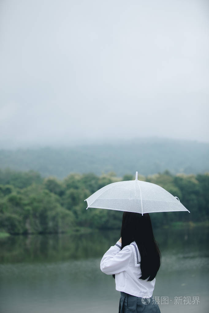 亚洲女孩的肖像,带着雨伞在雨中的自然人行道上散步