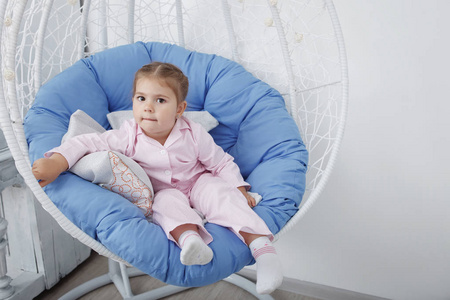 穿着粉色睡衣的可爱快乐的小女孩坐在秋千上的椅子上，枕头是蓝色的。