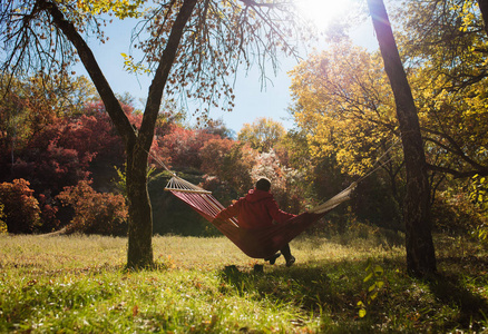 在金秋天，一个红衣男子坐在吊床上休息