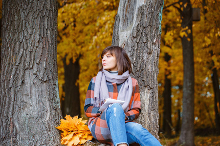 大学公园, 学习理念。秋天森林的年轻妇女的肖像。在笔记本中写入。褐发女郎妇女在秋季公园与时尚格子大衣和围巾