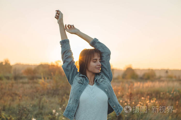 户外美容女孩在阳光照射下举起双手.美丽的少女模型女孩