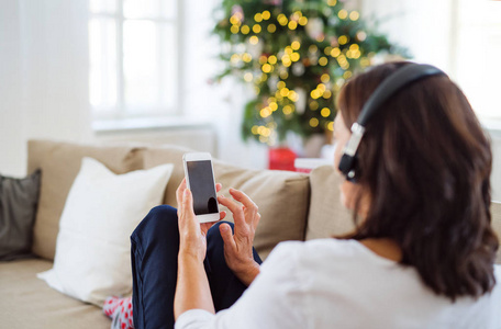 一个戴着耳机在圣诞节时在家听音乐的资深妇女