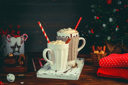 温馨的圣诞作文。两杯热饮料, 巧克力与奶油和卡布奇诺与肉桂棒在黑暗的木质背景。冷冬天的甜蜜款待