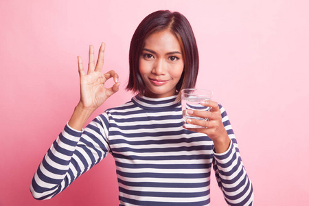 年轻的亚洲女人在粉红色的背景下可以喝一杯饮用水
