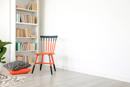 枕头旁边的橙色和黑色椅子在白色的房间内部，复制空间在空墙上。真实照片