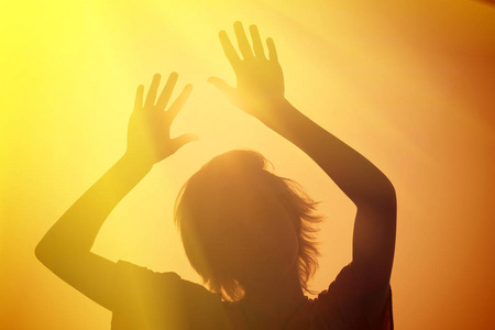 一个女孩的轮廓，举起双手对着太阳