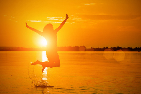 日落时分一个女人在水里跳跃的剪影