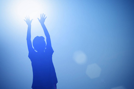 一个女孩的剪影，在蓝色背景上举起双手对着太阳
